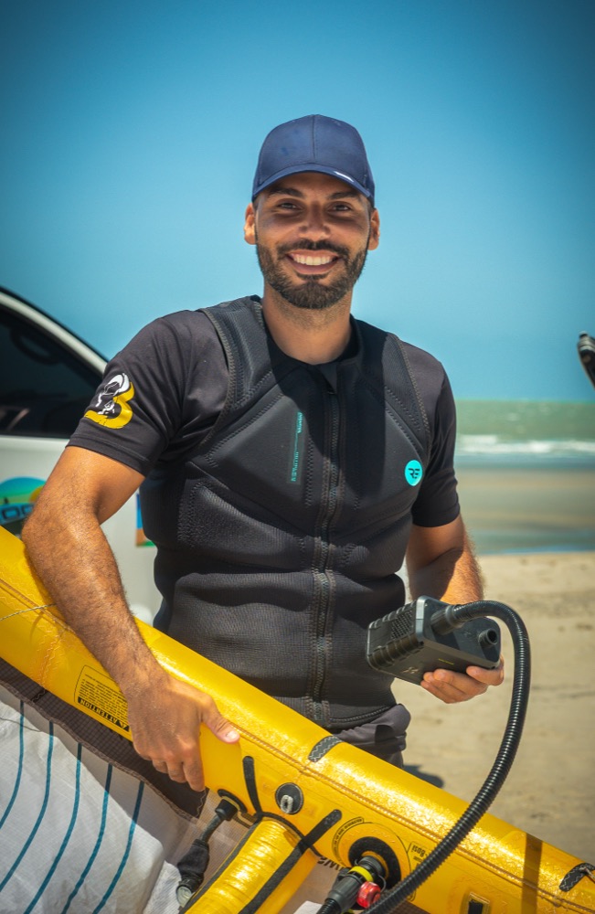 Arthur on the beach in a cap and impact vest, holding a camera rig