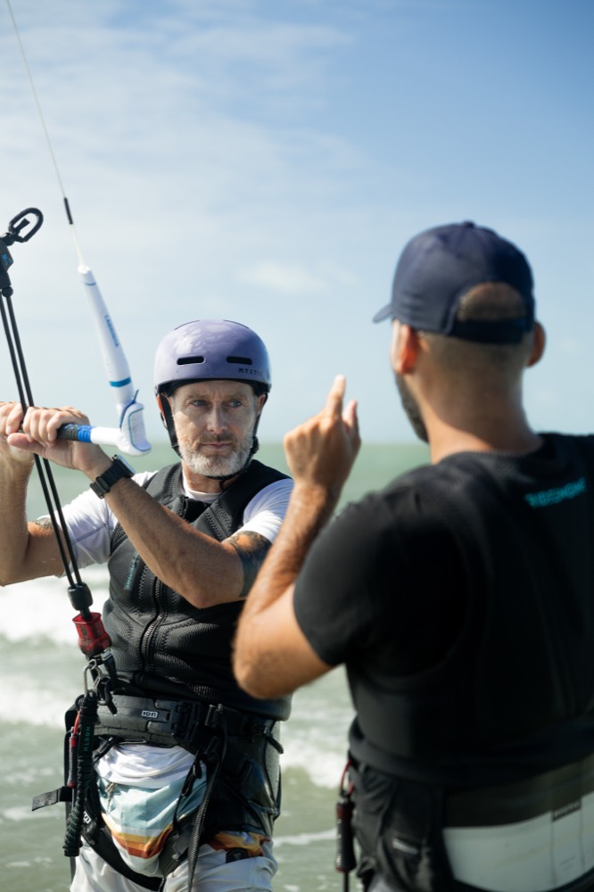 A coach giving hand signals to a rider holding the kite bar