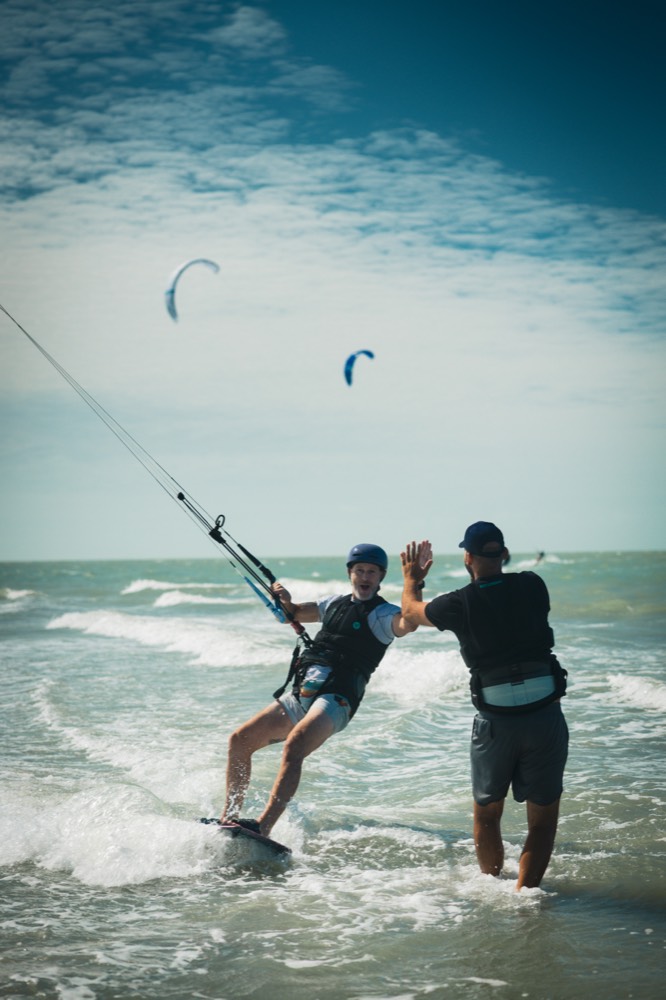 A rider high-fiving a coach in the waves off Preá