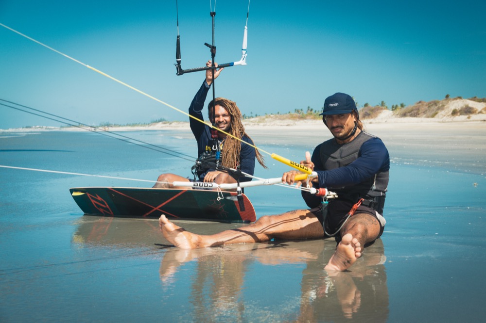 Two riders sitting at the water’s edge with their kites